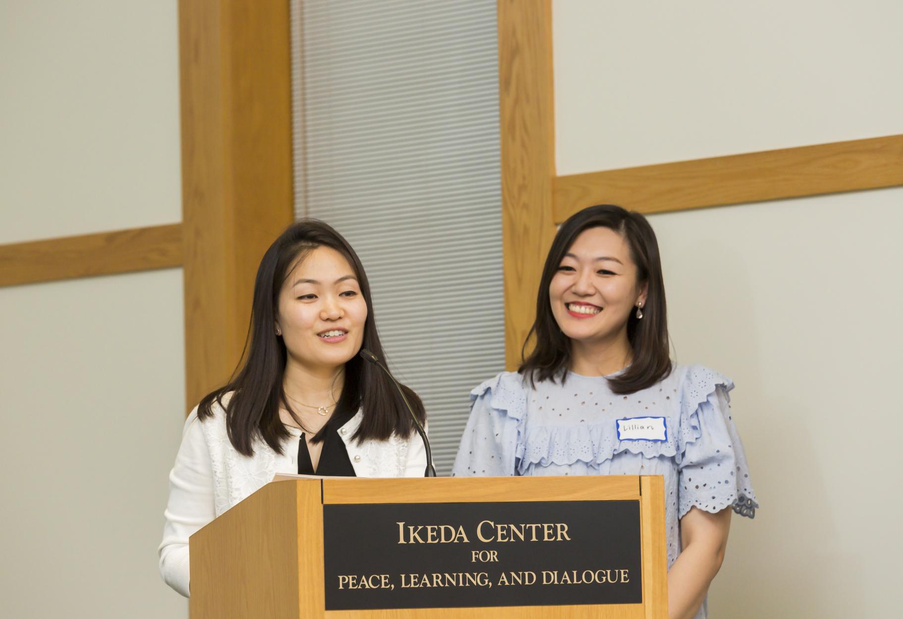 Staff members Anri Tanabe and Lillian I share opening words at the 2019 Ikeda Forum.